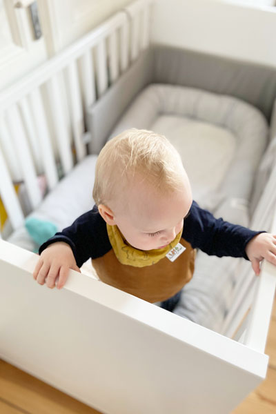 Baby Bente steht im Babybett Oscar von PAIDI.