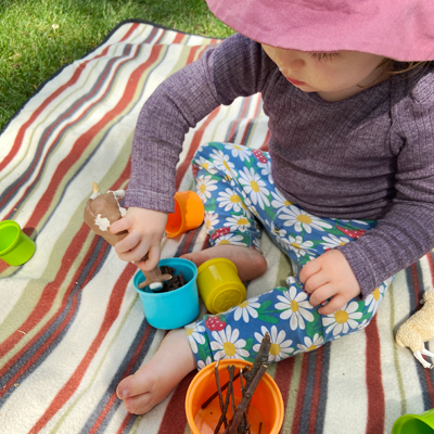 Kind spielt auf Picknickdecke mit Spielzeugkuh.