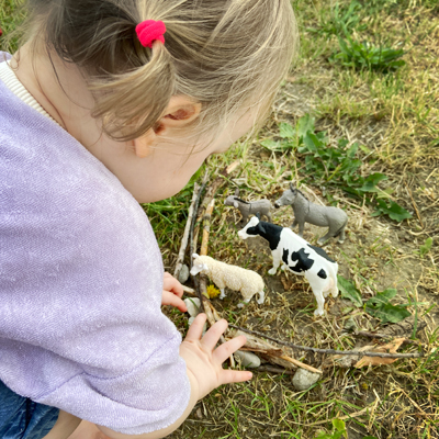 Kind spielt Bauernhof mit Tierfiguren und Zweigen.