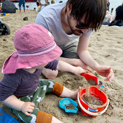 Vater und Kleinkind spielen im Sand.