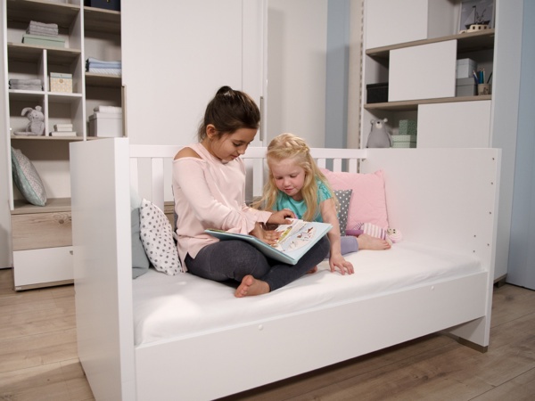 2 Mädchen sitzen auf umgebautem Kindersofa und blättern in Kinderbuch