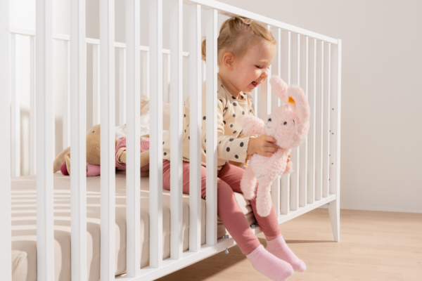 Ein Baby steigt aus dem PAIDI Babybettchen aus, die Schlupfsprossen sind offen.