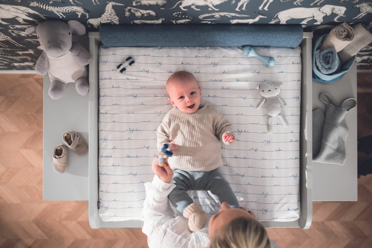 Baby liegt auf Wickelkommode und lacht glücklich.