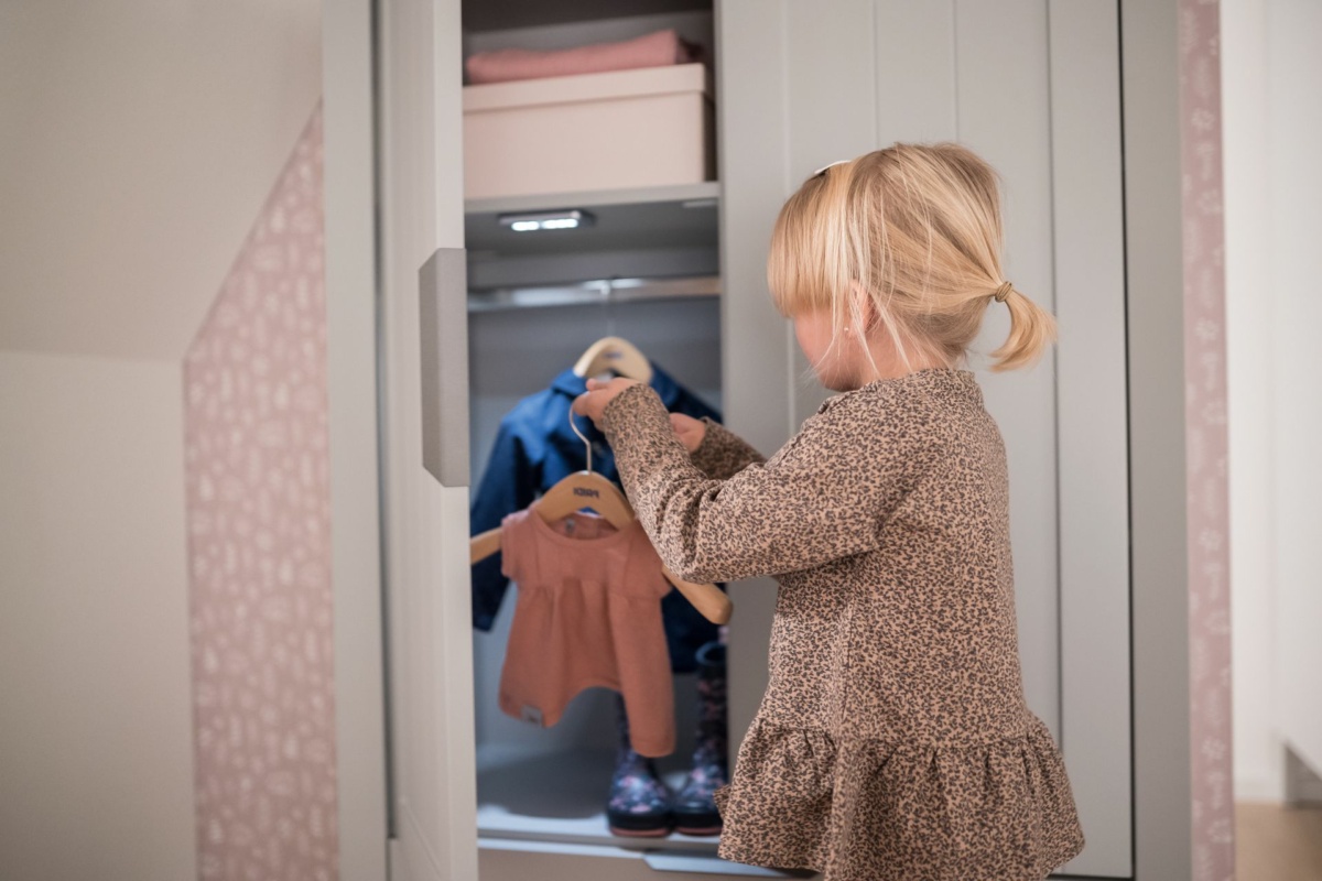 Kleines Mädchen räumt Kinderkleiderschrank ein.