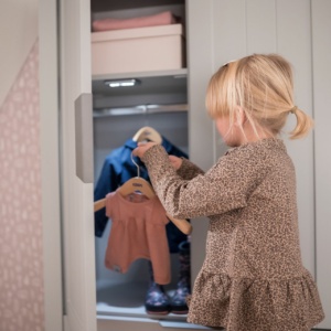 Kleines Mädchen räumt Kinderkleiderschrank ein.