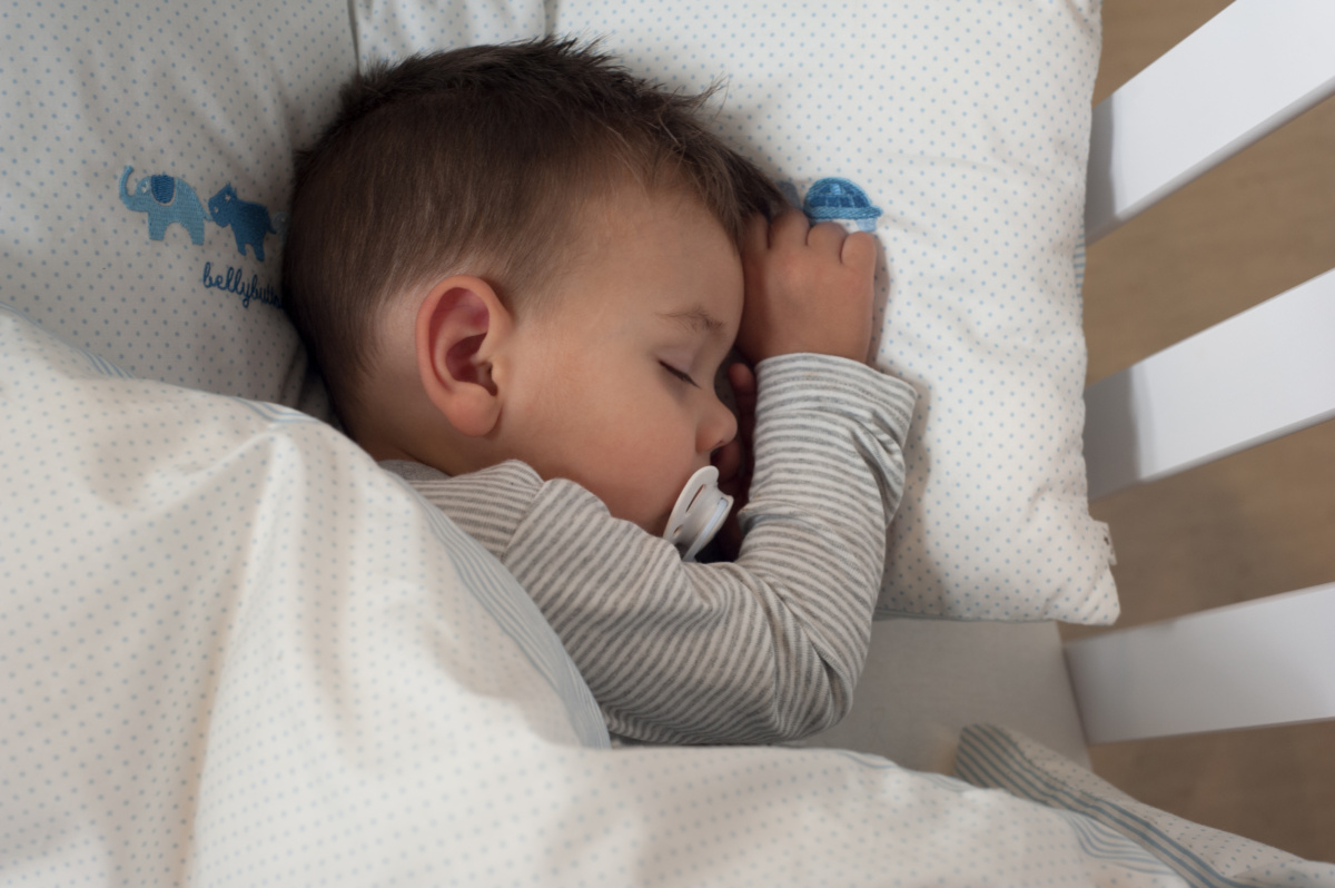 Einschlafrituale für Babys – Baby schläft auf der Seite mit Schnuller im Mund.