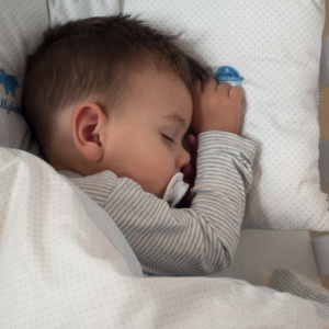 Einschlafrituale für Babys – Baby schläft auf der Seite mit Schnuller im Mund.