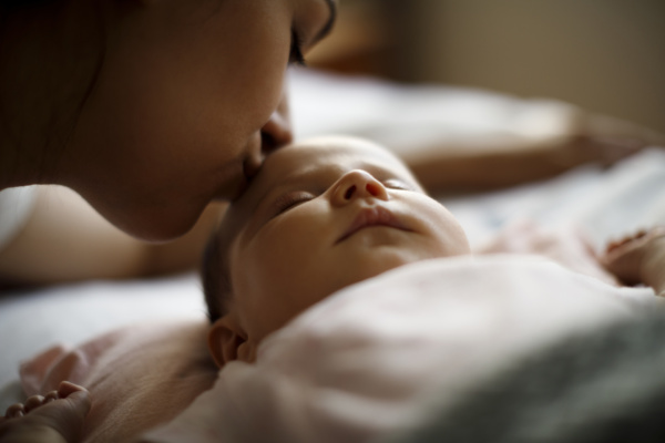 Einschlafrituale für Babys – Eine Mutter gibt ihrem Baby einen sanften Gute-Nacht-Kuss auf die Stirn.